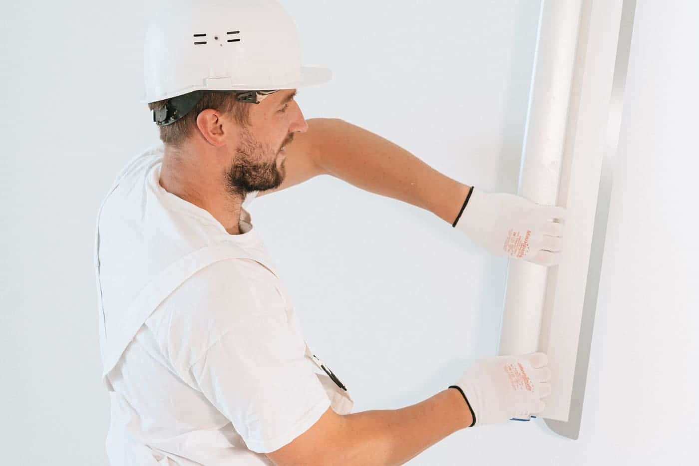 A worker in gloves and a hard hat fits a new drywall panel