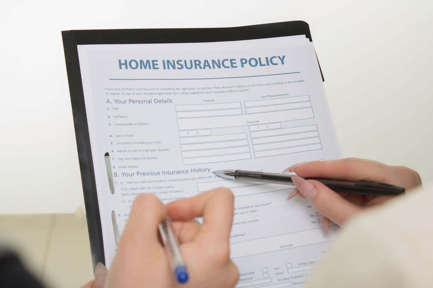 Hands filling out a home insurance claim form with a pen