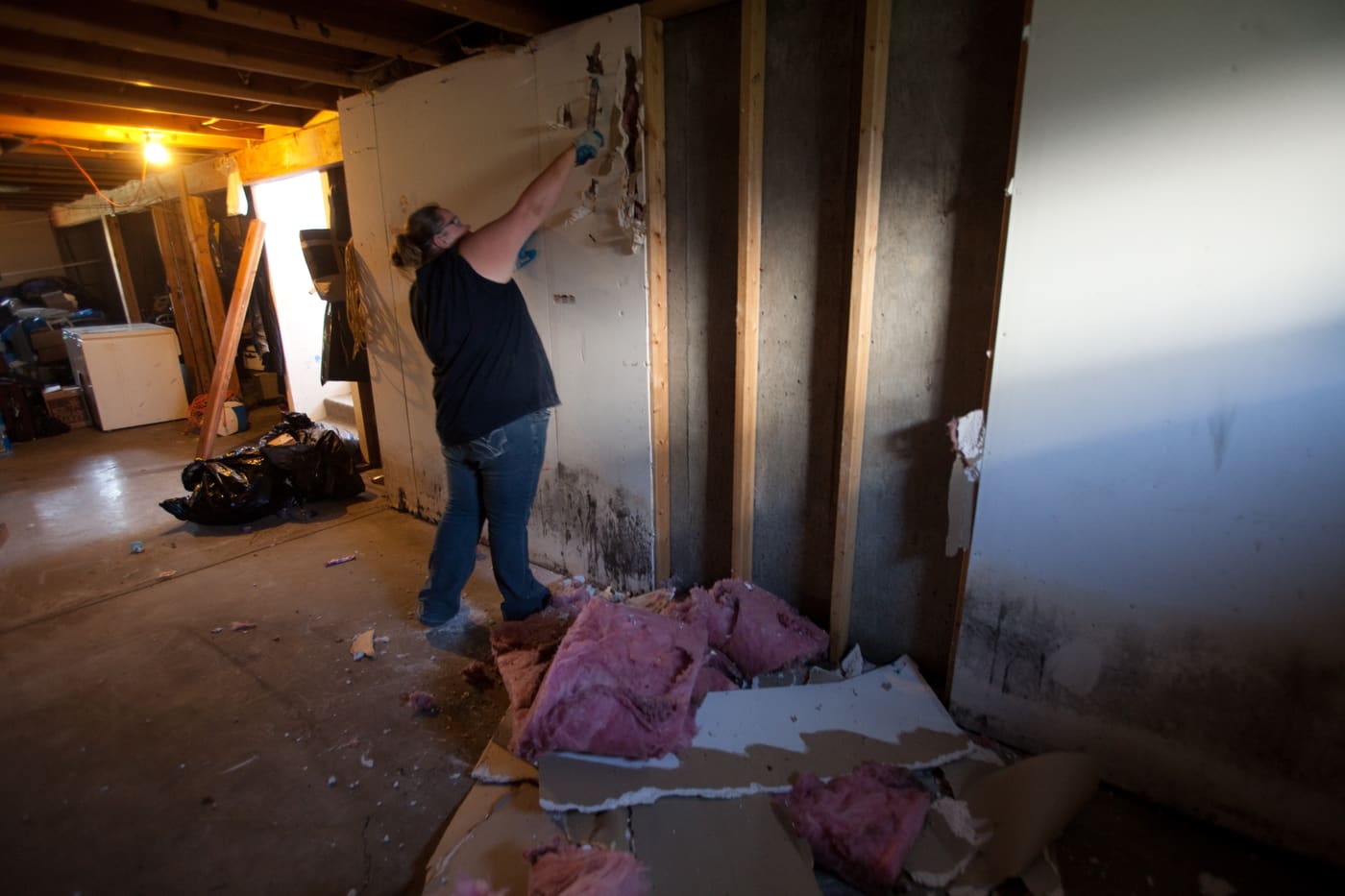 Homeowner tearing out water-damaged drywall and wet insulation down to the studs