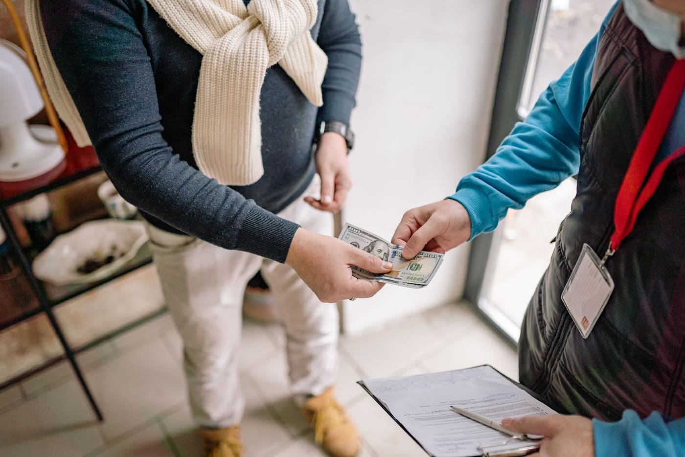 Homeowner handing hundred dollar bills to a contractor over a clipboard contract