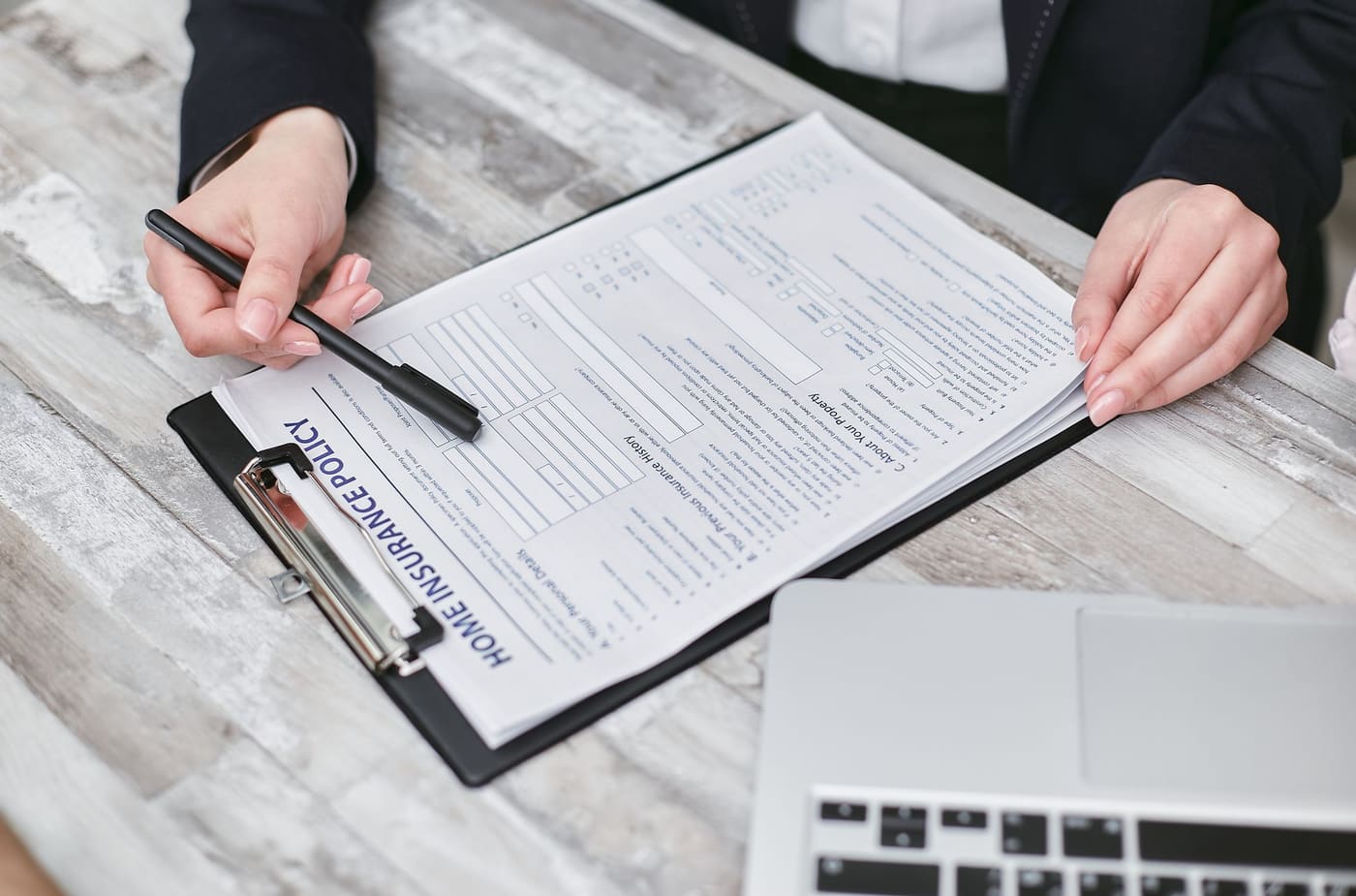 Contractor in business attire pointing a pen at a home insurance policy contract on a clipboard